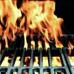 Flames rise through the grate of a barbecue grill